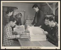 [recto] Assembling and folding the Sentinel, Heart Mountain Relocation Center newspaper, Bill Hosokawa, Editor, mothers his paper from editing and directing his reporters to seeing that they are wrapped and distributed properly to residents of Heart Mountain.