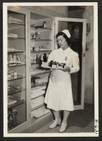 [recto] Miss Ruth Tanaka, a cadet nurse in the Seton Training School for Nurses, holds a tray of medicines in the ...
