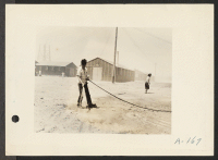 [recto] Poston, Ariz. (Site #1)--Jim Morikawa sprinkling in an attempt to settle the dust at this War Relocation Authority center for evacuees of Japanese ancestry. ;  Photographer: Clark, Fred ;  Poston, Arizona.