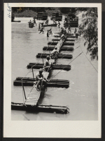[recto] Building a Pontoon Bridge. The sections are unloaded from trucks, assembled and put in the water, where they are hooked ...