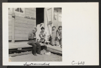 [recto] Father and son while away the hours carving small wooden animals for the children in front of their home in the barracks. They have been living at the Assembly Center for approximately one month. ;  Photographer: Lange, Dorothea ;  San Bruno, Californ