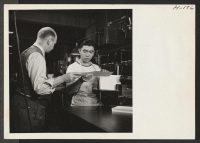 [recto] Ernest Shirakawa, a young evacuee from the Gila River Center is now employed by the Cuneo Press in Chicago, where he operates a book binding machine. He is shown here receiving his first check from the company's Pay Master. ;  Photographer: Mace, Charle