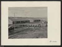 [recto] One of the last group of arrivals at the relocation center cross the warehouse area from the railroad platform to the registration office. ;  Photographer: Parker, Tom ;  Heart Mountain, Wyoming.