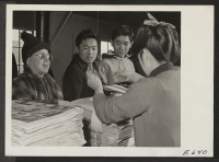 [recto] Customers line up at the counter as the Sentinel, Heart Mountain Relocation Center 8-page tabloid newspaper, is delivered. Center news ...