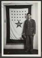 [recto] Yukiyasu Uyeoka, soldier of the United States army, stands before the Poston Relocation Center's service flag as one of the ...