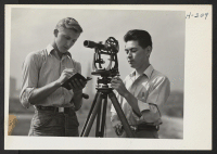 [recto] Henry Omachi (right) at the transit, a young student of engineering from the Tule Lake Center, now relocated in Cleveland and employed by the National Surveys Company, is here seen at work on the water front with Joe Semanisin, a Caucasian. ;  Photograp