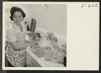 [recto] Mrs. Ayako Okubo is preparing pears for canning. Beside her on the sink are jars of canned pears and of ...