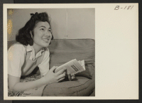 [recto] Lucy Yonemitshu, former student from Los Angeles, California, enjoys a pleasant afternoon with her book. Lucy lives with her parents in this barrack home, which has been very tastefully decorated by her father. ;  Photographer: Stewart, Francis ;  Man