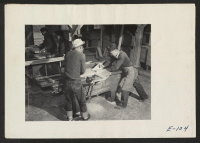 [recto] Evacuee workers operate a wood shaper in the wood shop where furniture for schools and recreational building at this relocation center are being [made]. ;  Photographer: Parker, Tom ;  Heart Mountain, Wyoming.