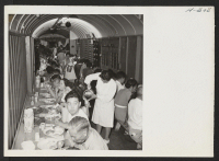 [recto] Dinner time in the improvised baggage car where transferees were fed by the Army enroute from Topaz to Tule Lake. The meals were excellent and the service, with volunteer help from among the passengers, was speedy and efficient. ;  Photographer: Mace, C