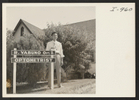[recto] Dr. Robert Yabuno, Optometrist, a graduate of the University of California, is shown standing beside his new sign post before ...