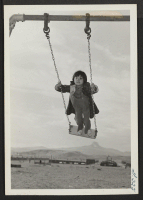 [recto] One of the young Heart Mountain school children is enjoying a swing on the center's play ground. ;  Photographer: Iwasaki, Hikaru ;  Heart Mountain, Wyoming.