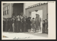 [recto] Japanese family heads and persons living alone form a line outside Civil Control station located in the Japanese American Citizens League Auditorium at 2031 Bush Street, to appear for processing in response to Civilian Exclusion Order No. 20. ;  Photogr