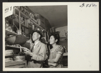 [recto] Mr. and Mrs. Harry Asaka weighing potatoes in their grocery store. Harry Asaka, Issei, first relocated to Washington, D.C., in ...