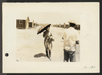 [recto] Poston, Ariz.--(Site #1)--This evacuee is fortified with an umbrella for protection from the sun, and high-top boots for strolling through the dusty streets at this War Relocation Authority center. ;  Photographer: Clark, Fred ;  Poston, Arizona.
